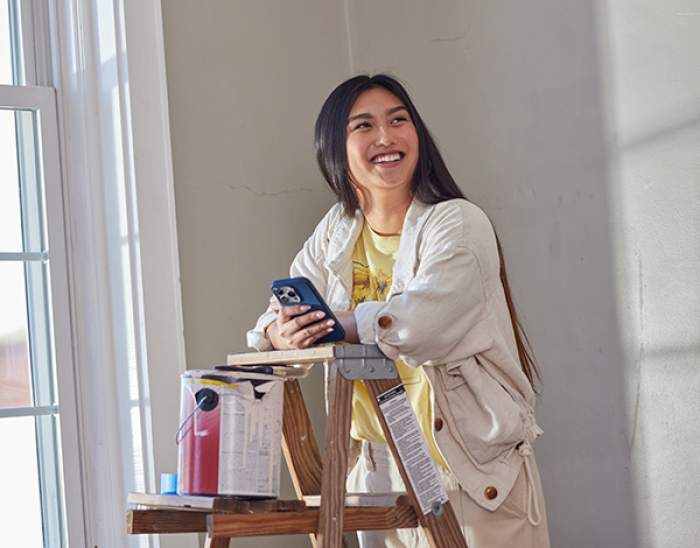 Girl on her phone smiling with painting supplies around her