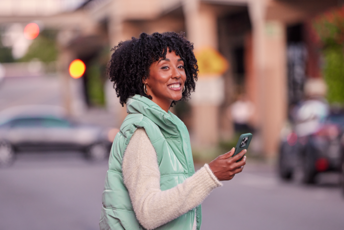 Girl walking through street with her phone smiling