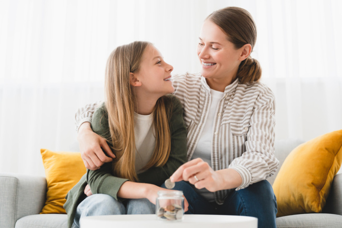 Mother and daughter sitting on couch smiling and adding change to a jar