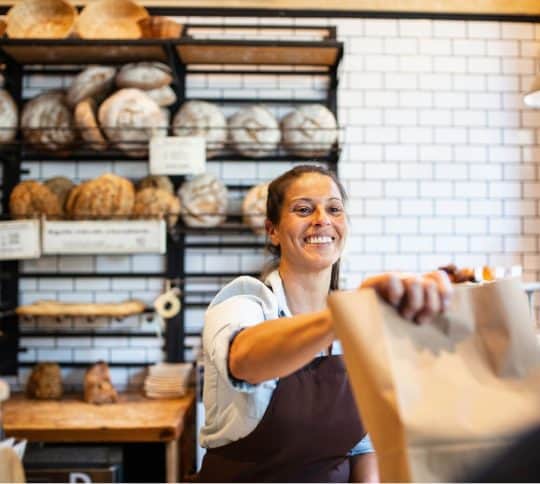 Woman handing brown bag over counter and smiling