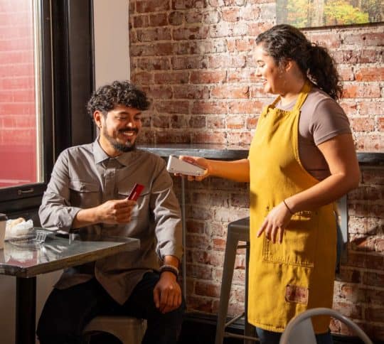 Coffee shop employee holding card reader up to a man to pay for his coffee
