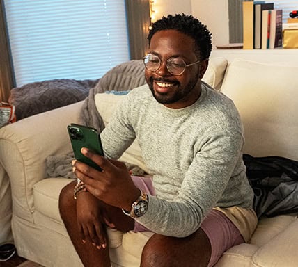 Man sitting on couch looking at his mobile phone and smiling
