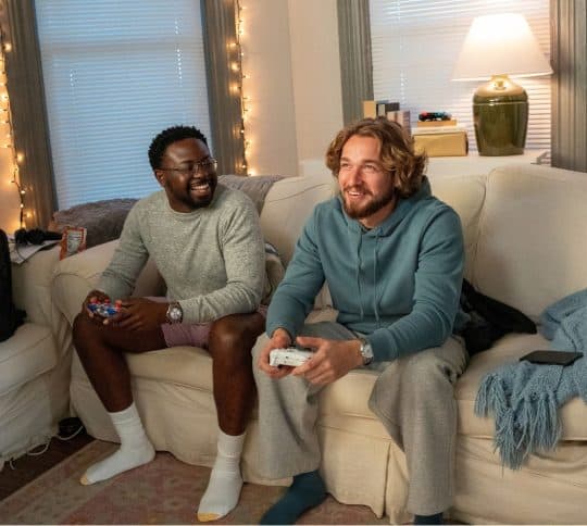 Two young college guys playing video games on the couch