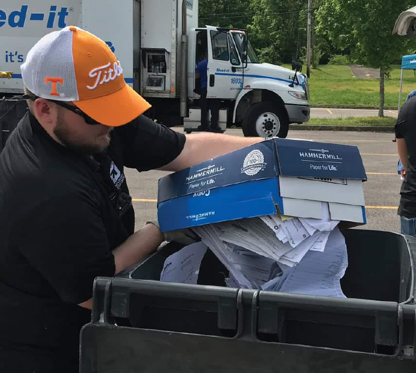 KTVAECU Staff member dumping a cardboard box of paper into a trashcan