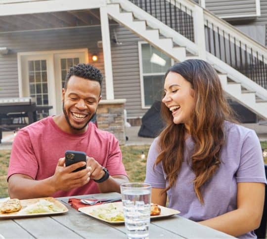 Young couple having a barbecue in their backyard laughing