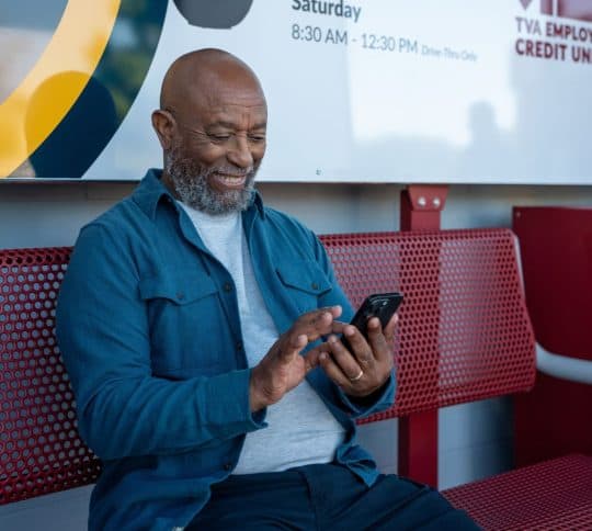 Man sitting on a bench smiling and checking his cell phone