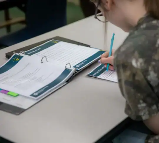 Teen in classroom filling out Financial Education worksheets