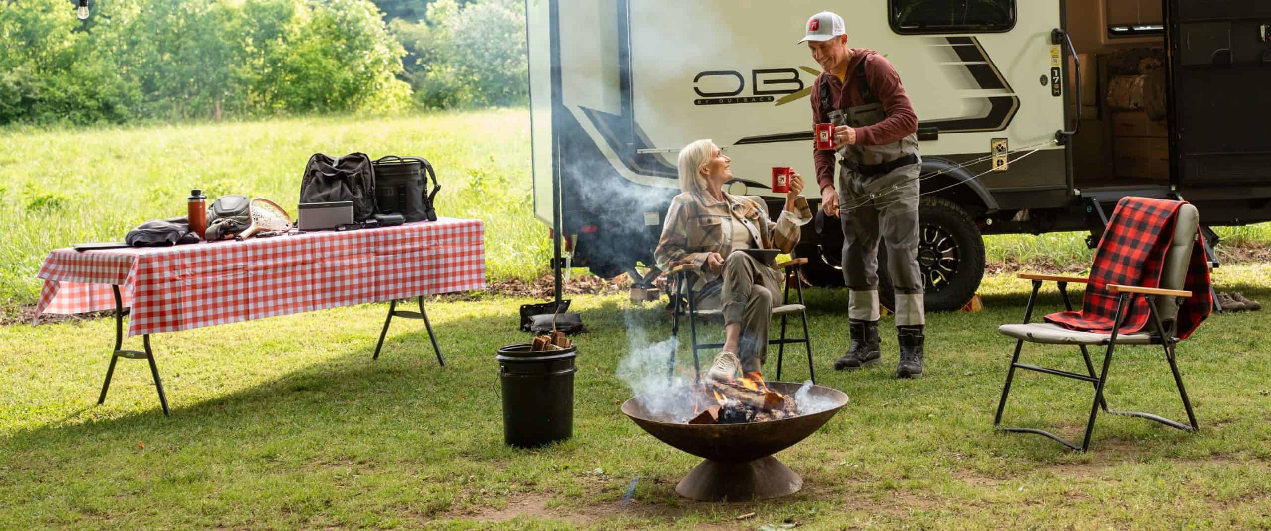 Man and woman holding up KTVAECU mugs at a campfire