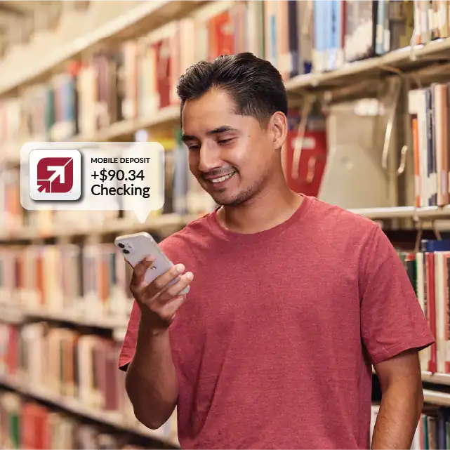 Man standing in library looking at cellphone