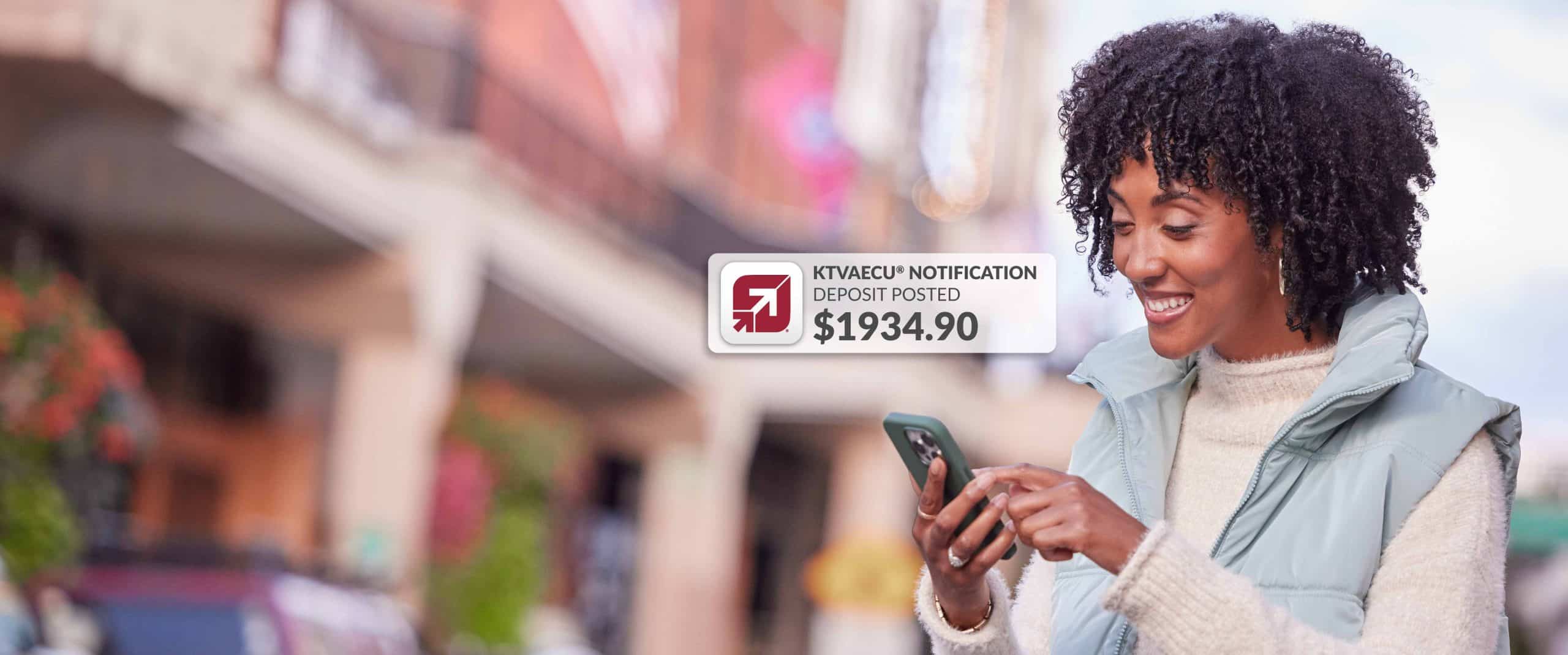 Young woman receives direct deposit notification on her phone while walking outdoors.
