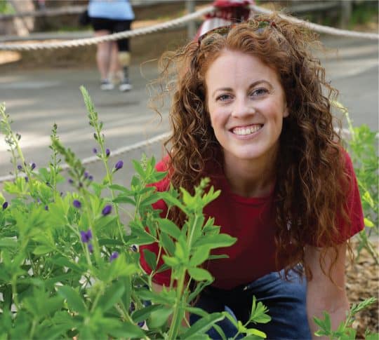 KTVAECU Staff Member smiling while kneeling down and planting herbs