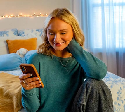 Young woman using smartphone in cozy bedroom setting.