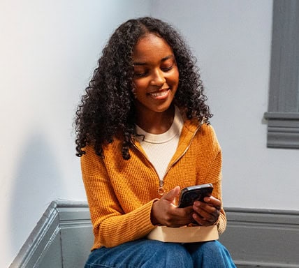 Young woman sitting on stairs and checking her phone.