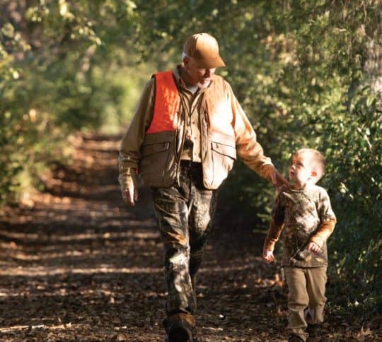 Man and boy dressed in camo walking down a trail path