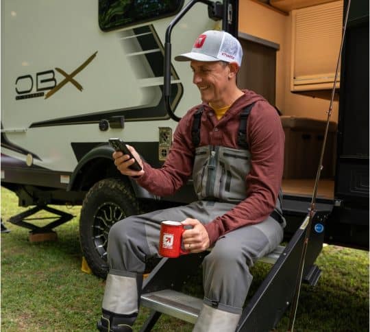 Man sitting on camper steps and looking at cell phone