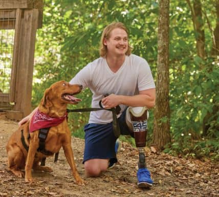 Man with above the knee amputation kneeling down the pet dog on a lead
