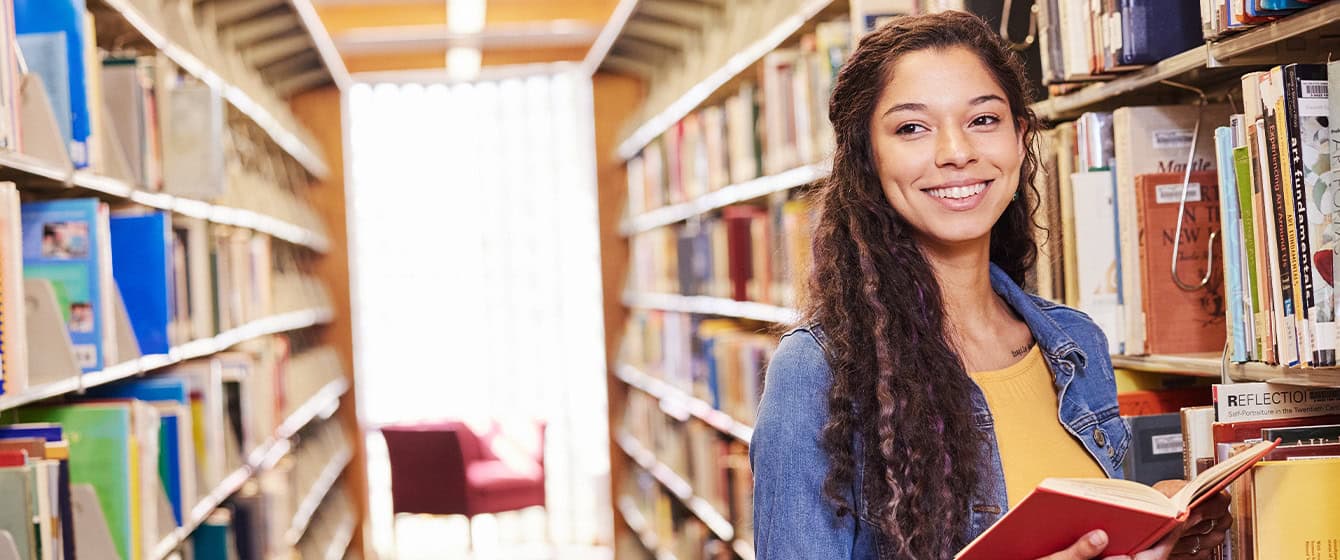 Young woman in library with an open book smiling