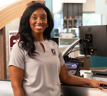 KTVA employee smiling at studio desk with equipment in background.